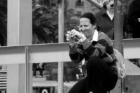 Eine Frau hockt auf dem Boden, hält einen Fotoapparat in der Hand und betrachtet kritisch ihre Aufnahme. Momentaufnahme des Alltags.